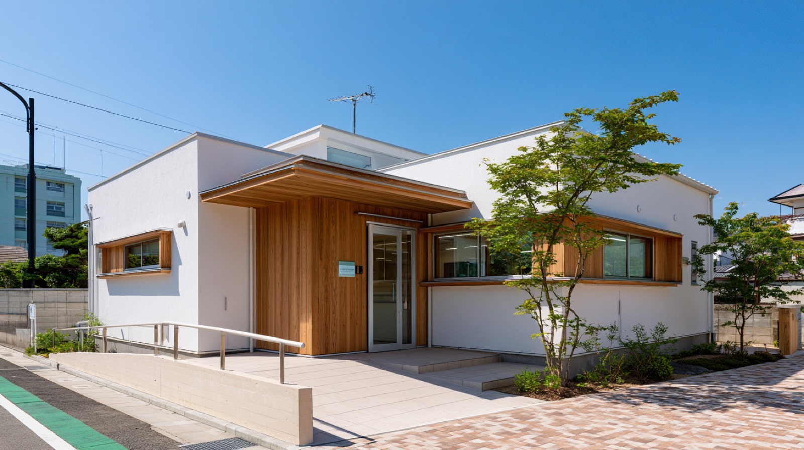 ひなた内科医院の外観。白壁と木のぬくもりのある建物で、入口にスロープと若葉が見えます。